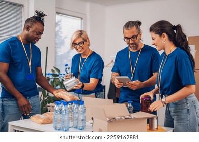 Multiracial volunteers working at charity organization and wearing blue t shirt while packing food grocery in donations box. Volunteering, social help for poor and needy. Copy space. - Powered by Shutterstock