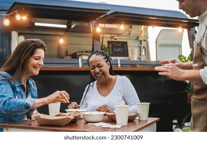 Multiracial women eating at food truck restaurant outdoor - Focus on african senior female face - Powered by Shutterstock