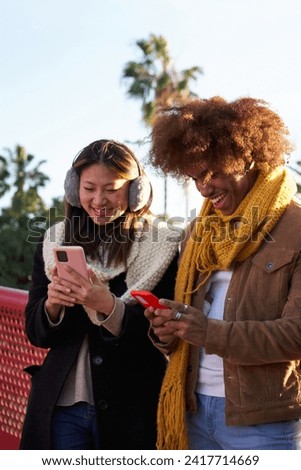 Multiracial young couple gathered outdoors using mobile phones cheerfully. Youth addicted to technology.