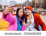 Multiracial young couple of lovers dating outdoors in winter using social media app on smartphone, wearing winter jackets and having fun - Multiethnic millennials bonding in a urban area