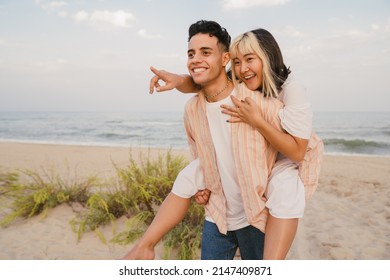 Multiracial young couple smiling while piggybacking on summer beach