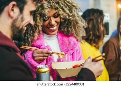 Multiracial young friends eating takeaway food outdoor - Focus on african girl chopsticks - Powered by Shutterstock