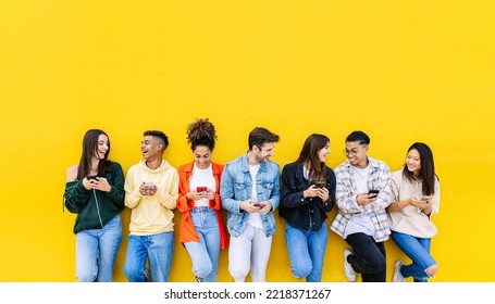 Multiracial young friends having fun sharing media content on mobile phone - Millennial diverse people using smart phone together leaning against wall - Social media trends and technology concept - Shutterstock ID 2218371267