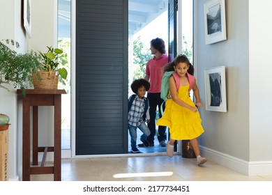 Multiracial Young Man Standing At Entrance While Children With Backpacks Running Inside House. Unaltered, Family, Togetherness, Childhood, Student, School And Lifestyle Concept.