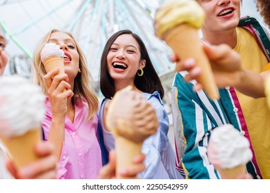 Multiracial young people together meeting at amusement park and eating ice creams - Group of friends with mixed races having fun outdoors - Friendship and lifestyle concepts