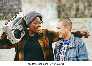Multiracial young women dancing outdoor with urban background - Trendy street wear style and friendship concept - Focus on african female face - Powered by Shutterstock