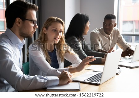 Multiracial younger and older colleagues working in pairs in office. Skilled female employee explaining focused male coworker new software. Confident manager discussing project details with client.