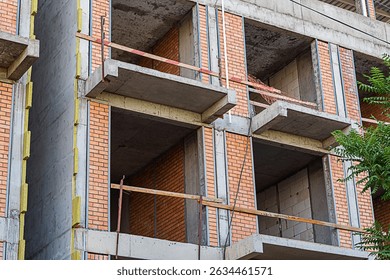 Multi-storey building during construction work. Load-bearing elements of structure made of high-class concrete, red brick, fine meshed aerated block. Facade insulated with sheet of mineral basalt wool