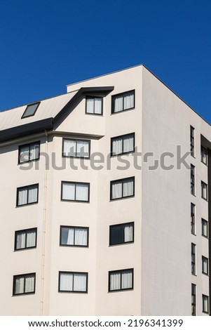 A multi-storey white building with identical windows against a blue sky.