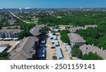 Multistory apartment buildings with covered parking near lush greenery suburban park along Baird Farm Road in North Arlington, Texas, water tower, city stadium in background, master planned area. USA