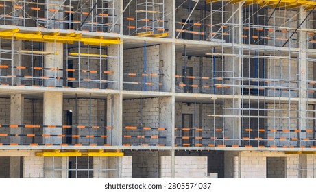 Multi-story building construction progresses with visible concrete pillars. Yellow scaffolding supports each floor level. The structure is under development in an urban area