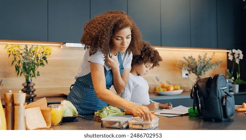 Multitask, phone call and woman in kitchen with child, packing lunch and routine in morning. Mother, kid and talk on mobile in home for communication, care and healthy meal for son in kindergarten - Powered by Shutterstock