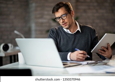 Multi  tasking businessman working in the office  He is using touchpad while reading an e  mail laptop   taking notes the paper 