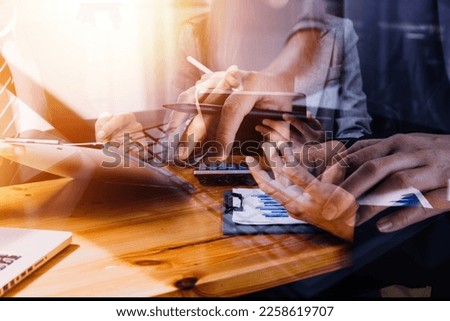Multi-tasking businessman working in the office. He is using touchpad while reading an e-mail on laptop and taking notes on the paper.