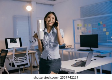 Multitasking businesswoman in a modern office. Holding a coffee mug and chatting on her smartphone confidently. Surrounded by technology and a sleek laptop - Powered by Shutterstock