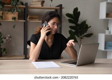 Multitasking. Busy hispanic female make business call from workplace to discuss with client colleague document contract agreement on laptop screen. Young businesswoman talk by phone doing online work