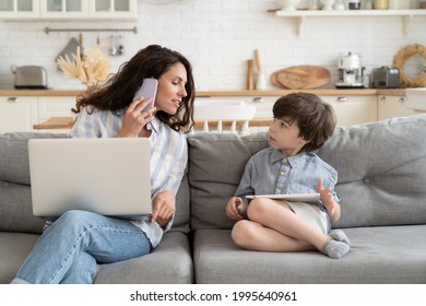 Multitasking casual businesswoman and mother work from home talk to kid, make phone call use laptop sit on couch in kitchen. Modern mom remote worker or freelancer lifestyle during covid-19 lockdown - Powered by Shutterstock