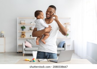 Multitasking Concept. Young Black Man Holding Little Baby And Talking On Cellphone While Working Remotely With Laptop At Home, African American Freelancer Guy Enjoying Paternity Leave, Copy Space