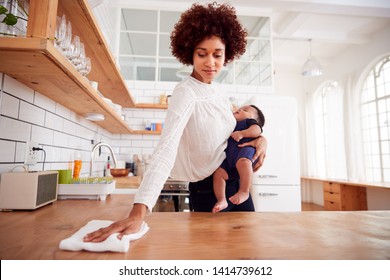 Multi-Tasking Mother Holds Sleeping Baby Son And Cleans In Kitchen - Powered by Shutterstock