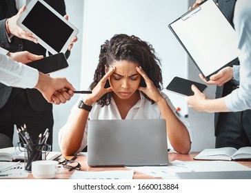 Multitasking. Overworked Afro Businesswoman Sitting Touching Head Ignoring Colleagues Tired Of Multiple Tasks At Work In Modern Office.
