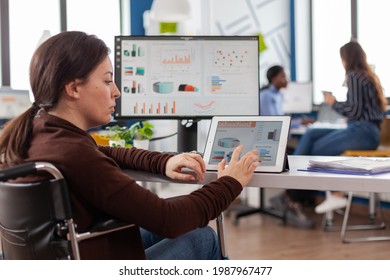 Multitasking paralyzed project manager, businesswoman with disabilites invalid immobilized woman using computer and tablet in same time working in business start-up office sitting in wheelchair.