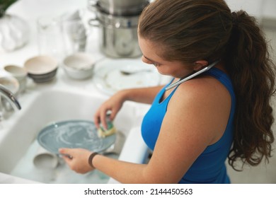 Multitasking Is Second Nature To Her. Shot Of A Woman Talking On A Cellphone While Washing Dishes.