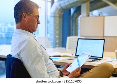 Multitasking with wireless efficiency. Shot of a focussed businessman using his tablet while sitting at his desk in the office.