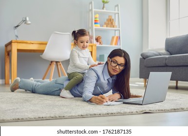 Multitasking for work at home moms. Young woman doing online job on laptop while her daughter sitting on her back - Powered by Shutterstock