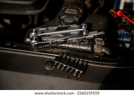 A multi-tool with various attachments is placed on a car engine, highlighting its utility for automotive repairs, with a set of interchangeable bits nearby.