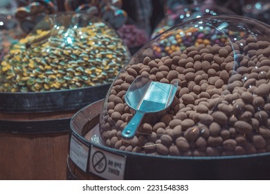 A multitude of round chocolate bonbons in a plastic dispenser with a spoon or shovel to take them out. Candy shop scene. - Shutterstock ID 2231548383