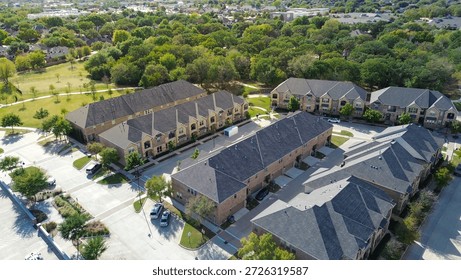 Multi-unit homes and white moving container near curved drive and tree canopy off Old Settlers Road. Brick walls, asphalt roofs reflect winter light across landscaped medians, Flower Mound, Texas. USA