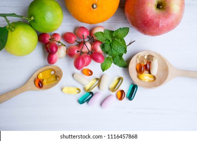 Multivitamin Supplements From Fruit On White Wood Background With Wooden Spoon.