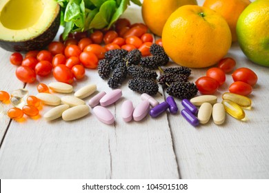 Multivitamins with fresh fruits on white wood.