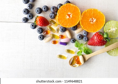 Multivitamine und Supplemente mit frischen und gesunden Früchten auf weißem Holzhintergrund.