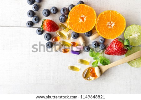 Multivitamins and supplements with fresh and healthy fruits on white wooden background.