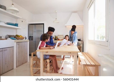 Mum And Dad Help Their Kids With Homework At Kitchen Table