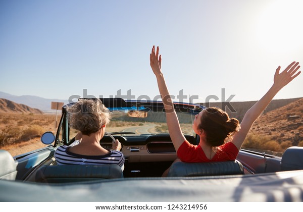 Mum driving car, daughter with hands in the air,\
back view