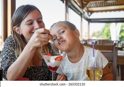 Mum Feeds The Daughter Delicious Sweet Ice Cream With Strawberries In A Restaurant. Shallow Depth Of Field. Focus On The Child's Face.