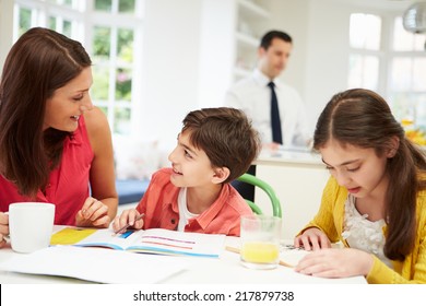 Mum Helps Children With Homework As Dad Works In Background