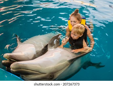 Mum with kid floats with dolphins in pool