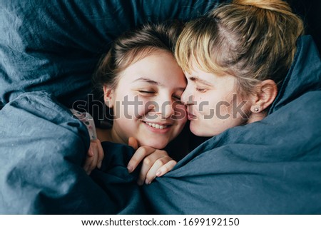 mum kissing daughter in the mother day morning. Portrait of light hair family under the blanket together in soft morning light on blue linen bed. Concept of happy family living, relaxation and joy