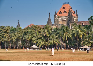 Mumbai, India - January 04, 2020: High Court Of Bombay Seen From Oval Maidan Rising Beautifully To The Sky, Surrounded By Palm Trees, And A Crowd Of Local People Playing Cricket, In The Day.