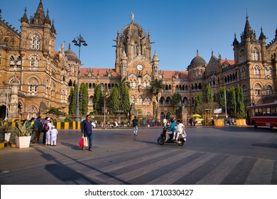 Mumbai, India - January 04, 2020: Some People Waiting In The Street At Chhatrapati Shivaji Maharaj Terminus Train Station, Surrounded By Big Buildings And Towers, While Others Are Driving, In The Day.