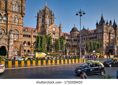 Mumbai, India - January 04, 2020: Some People Waiting In The Street At Chhatrapati Shivaji Maharaj Terminus Train Station, Surrounded By Big Buildings And Towers, While Others Are Driving, In The Day.