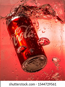 Mumbai, Maharashtra, India - 10/28/2019: A Can Of Coke Splashes In Water With Bubbles On A Red Background.