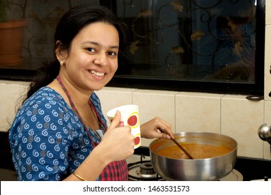 Mumbai, Maharashtra, India- Asia, Aug; 2; 2008 - Attractive Young South Asian Indian Woman Drinking Tea, Wearing Apron In Kitchen And Cooking Vegetables 