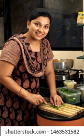 Mumbai, Maharashtra, India- Asia, Aug; 2; 2008 - Attractive young South asian Indian woman Smiling cutting coriander on a cutting board With knife in kitchen.