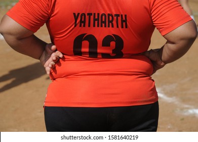 Mumbai, Maharashtra, India- Dec. 2019 -  Unidentified Indian Young Fat boy watching Football game, Back view of a boy Standing on a open ground Wearing Red T shirt.    