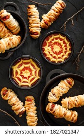 Mummy Dogs And Ketchup-mustard Sauces On A Black Background  Top View. Halloween Food Idea For  Party 