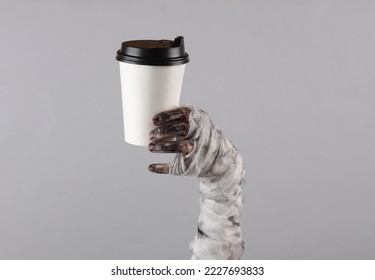 Mummy hand holding coffee cup isolated on gray background. Halloween concept - Powered by Shutterstock